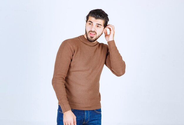 Photo of a young attractive man model standing and looking away over white wall. High quality photo