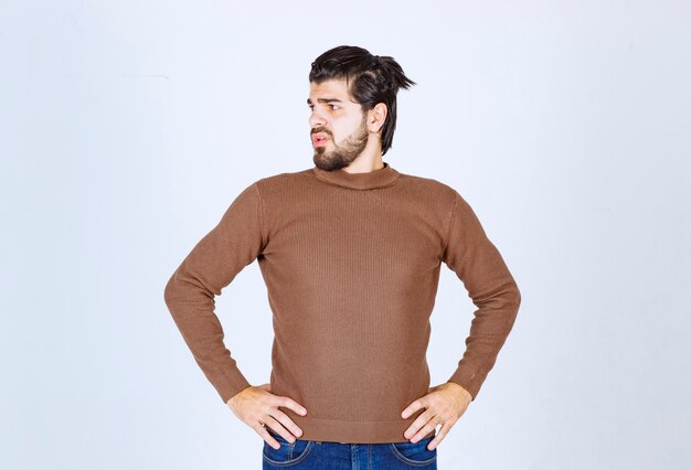 Photo of a young attractive man model standing with hands on hips and looking away over white wall. High quality photo
