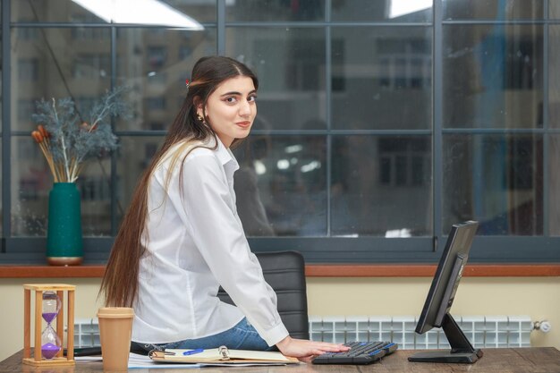 The photo of a young beautiful lady sitting at the desk and smiling