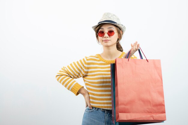 Фотография молодой брюнетки в солнечных очках, держащей сумки с покупками. Фото высокого качества