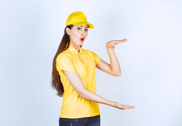 Photo of young deliverywoman holding open space over white wall.