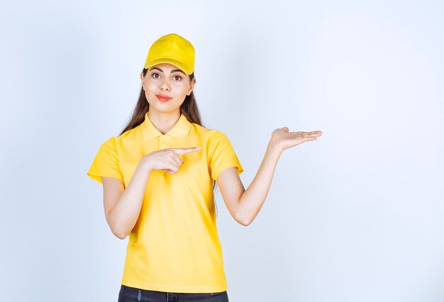 Photo of young deliverywoman holding open space over white wall.