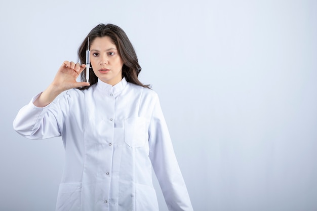 Photo of young doctor with syringe standing on grey. 