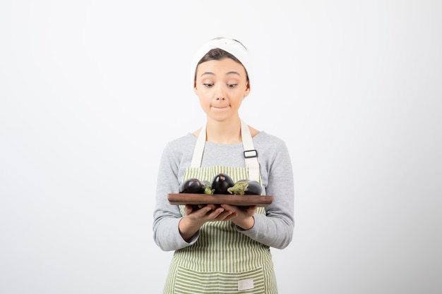 Photo of young female cook looking at plate of eggplants on white 