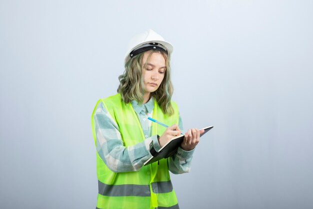 Photo of young female engineer writing her ideas on notebook over white wall. High quality photo