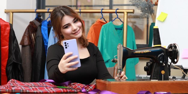 Photo of young female tailor taking selfie at the atelier