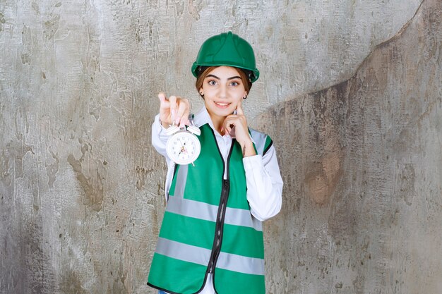 Photo of young girl in green vest and hardhat holding alarm clock