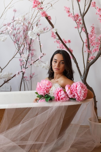 Photo of young lady sittin in a bathtub and holding pink beautiful flowers High quality photo