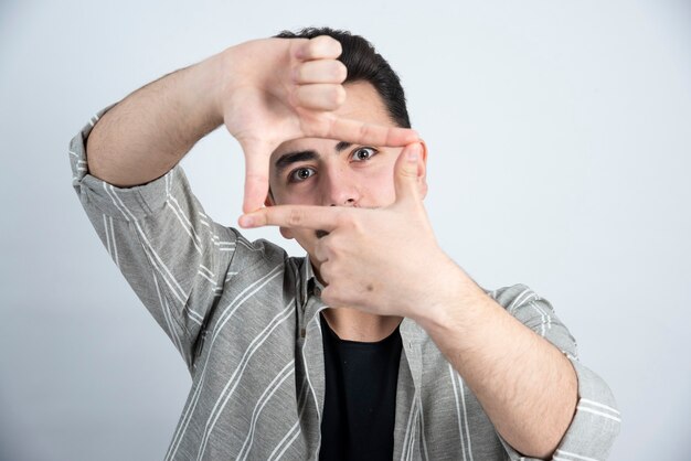 Photo of young man in casual clothes posing to camera over white wall.