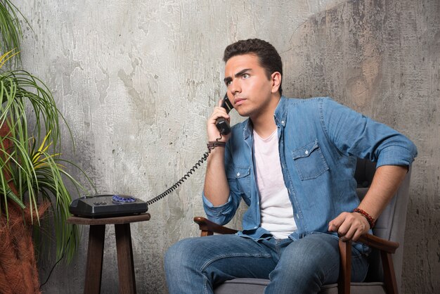Photo of young man talking on phone and sitting on chair . High quality photo
