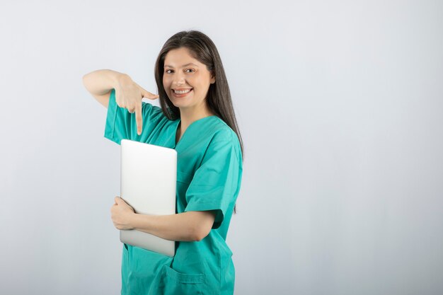 Photo of young nurse pointing at laptop on white. 