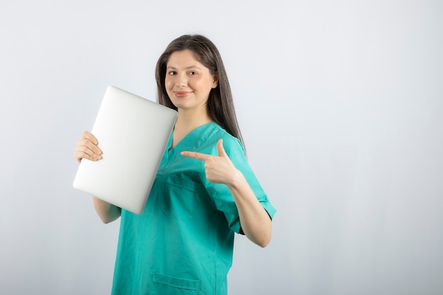 Photo of young nurse pointing at laptop on white. 