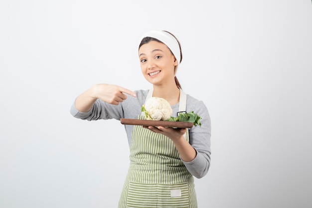 Photo of a young pretty woman model pointing at a wooden plate with cauliflower 