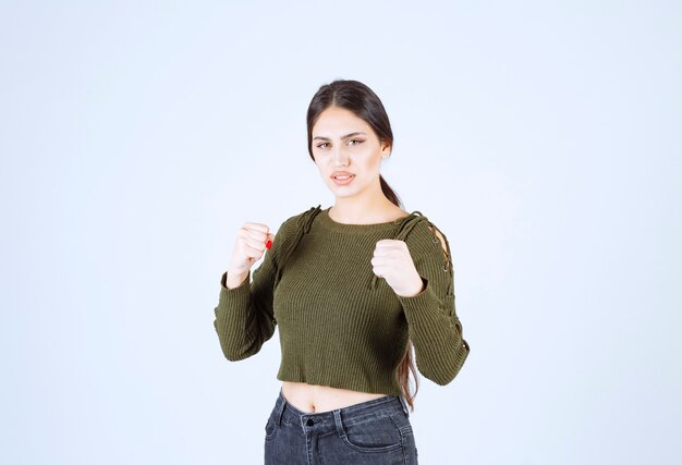 Photo of a young serious woman model showing her fists over white wall.