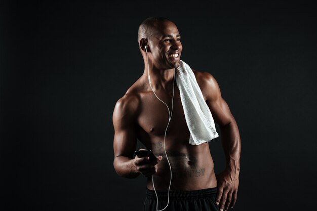若い笑顔の写真アフロアメリカンスポーツ男タオルを保持しているタオルで音楽を聴く