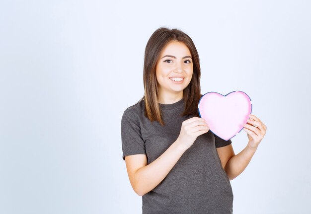 Photo of young smiling woman holding a heart shaped gift box.