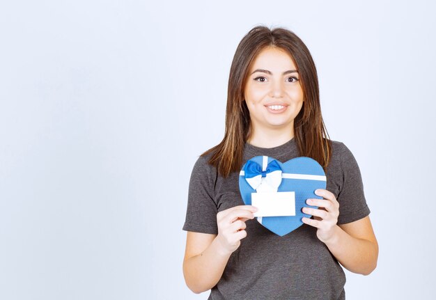 Photo of young smiling woman holding a heart shaped gift box.