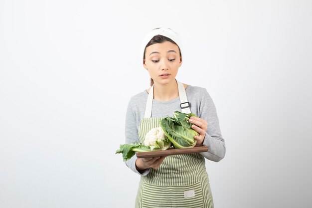 カリフラワーと木の板を保持しているエプロンの若い女性の写真