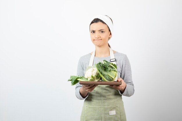 Photo of a young woman in apron holding a wooden plate with cauliflowers