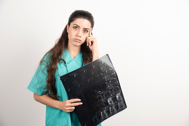 Фотография доктора молодой женщины держа рентгеновский снимок над белой стеной.