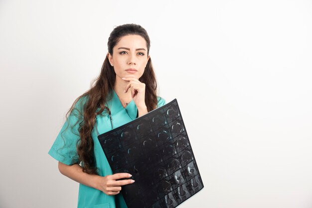 Photo of a young woman doctor holding x-ray over white wall.