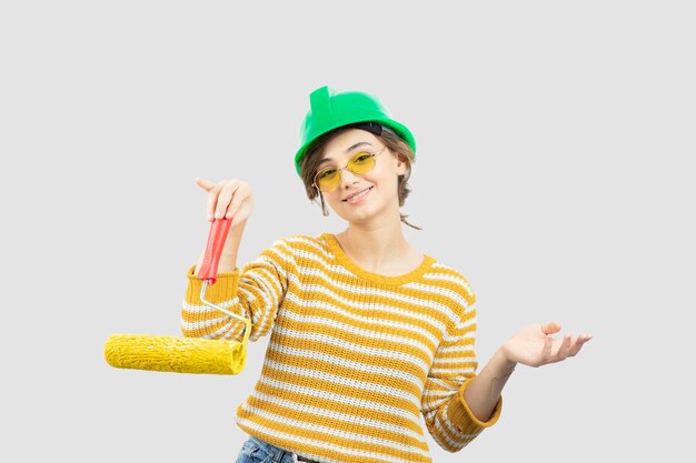 Photo of young woman in green safety helmet holding a paint roller in her hand . High quality photo