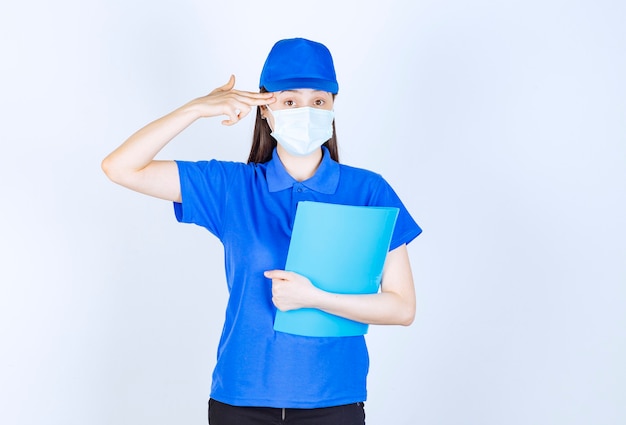 Фото молодой женщины в медицинской маске, держа папку и указывая пальцем на ее голову.