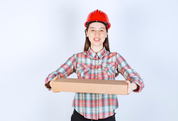 Photo of young woman in red helmet holding carton box. 