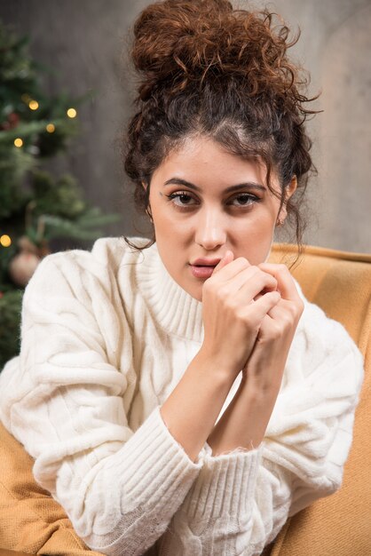 Photo of young woman sitting in comfy chair near Christmas tree