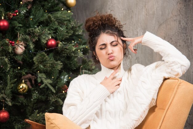 Photo of young woman sitting in comfy chair near Christmas tree