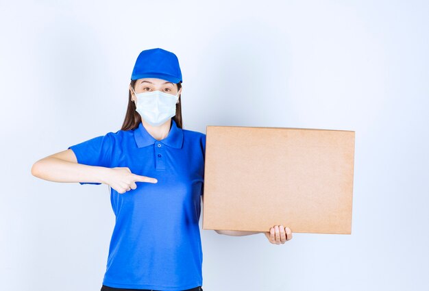Фото молодой женщины в форме и медицинской маске, указывая на бумажную коробку.