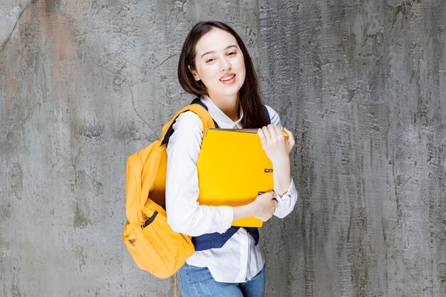 Фотография молодой женщины с желтым рюкзаком, стоящей над стеной. Фото высокого качества