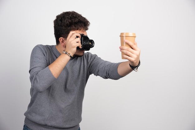 Foto gratuita fotografa tenendo in mano una tazza di caffè in plastica per scattare foto.