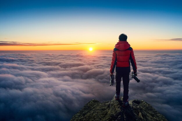 カメラを持って、雲の上の視点に立っている写真家の手。日の出のパノラマの視点。