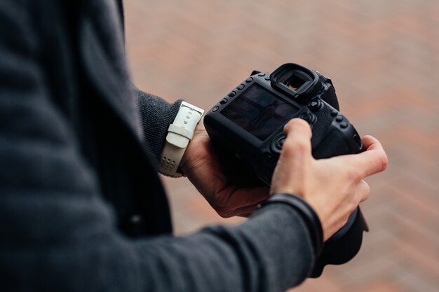 Photographer holding professional camera looks at photos, outdoors.