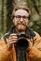 Foto gratuita uomo del fotografo che sorride mentre tiene la macchina fotografica nel bosco