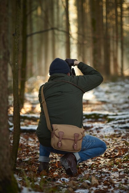 눈과 잎으로 덮여 녹지로 둘러싸인 숲에서 사진을 찍는 사진 작가