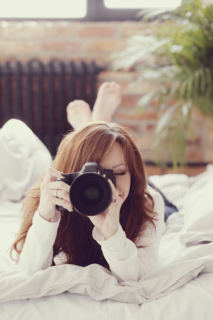 写真カメラでベッドに横たわっている写真家女性