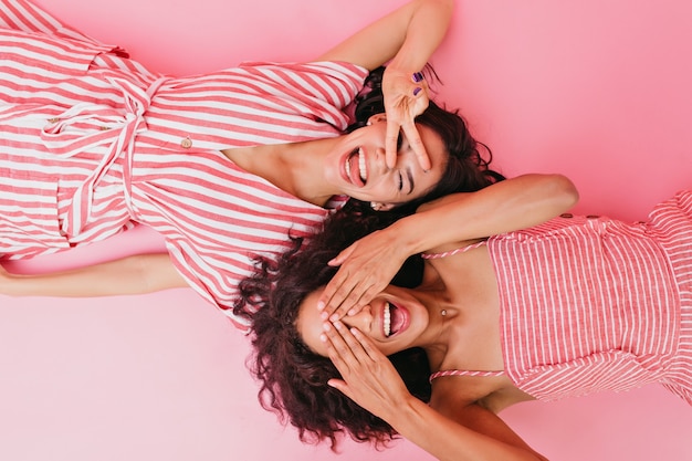 Free photo photos of two young and chatming girls in beautiful dress and bright striped sundress, smiling and closing their eyes