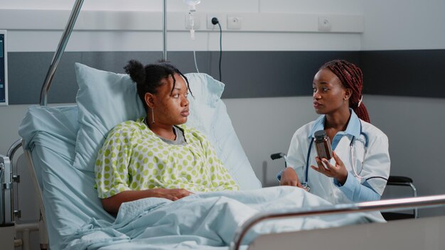 Physician holding bottle of pills to give to sick patient in hospital ward. Young woman with disease receiving prescription treatment with flask of medicine from healthcare specialist