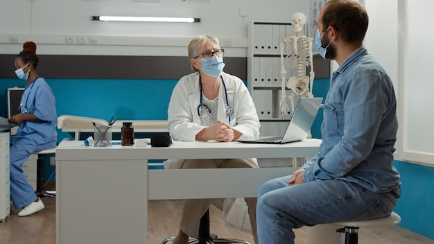 Physician and male patient having conversation at medical examination in cabinet. Doing health care consultation at checkup appointment to give support and prescription medicine during pandemic.