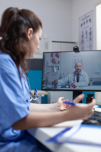 Physician nurse discussing virus symptoms with remote doctor during online videocall meeting conference during clinical consultation in hospital office. Telemedicine call on computer screen