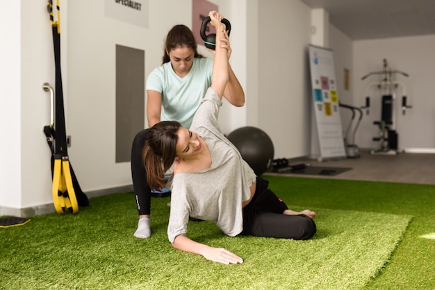 Physiotherapist assisting young caucasian woman with exercise with dumbbell