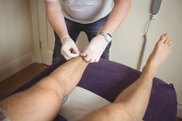 Физиотерапевт выполняет сухую иглу на ноге пациента