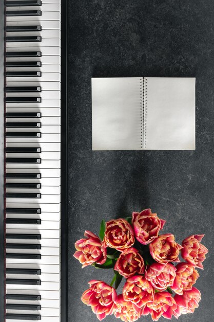 暗い背景のトップビュー上のチューリップの花とノートパッドのピアノの花束