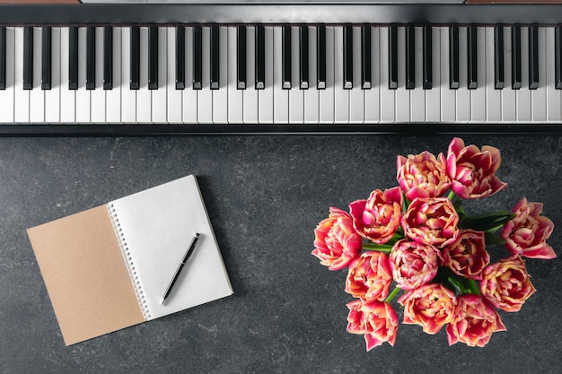 暗い背景のトップビュー上のチューリップの花とノートパッドのピアノの花束