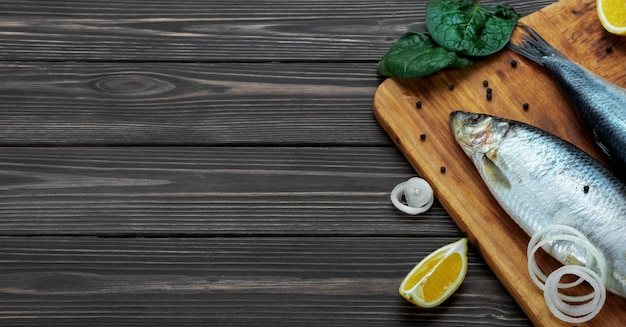 Pickled atlantic herring fishes on a cutting board next to spices and lemon