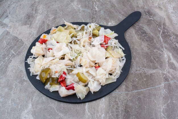 Pickled cabbage with various vegetables on dark board.