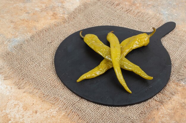 Pickled chili peppers on black board with burlap