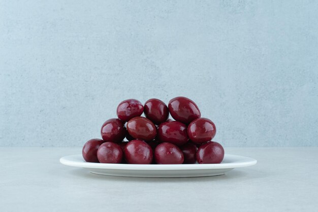 Маринованные кизиловые вишни на белой тарелке.
